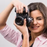 Eine Fotografin hält sich eine Kamera vors Gesicht und macht ein Bild, wahrscheinlich ein Portraits